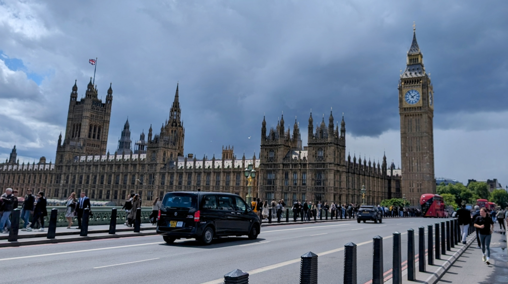 Taxi on bridge driving past Houses of Parliament in the background.